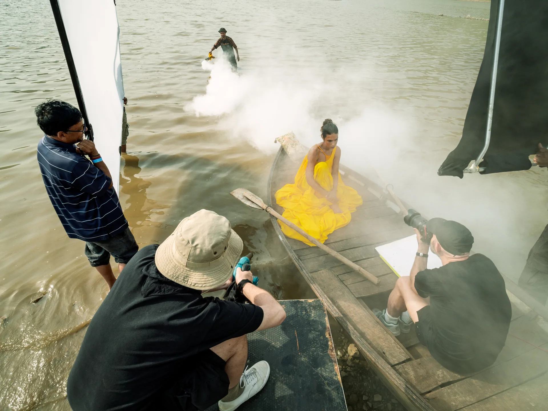 Model in gelbem Kleid in einem Boot, umgeben von Nebel und Fotografen